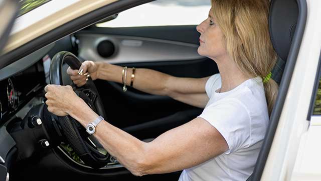 Taxifahrerin macht Rückenübung im Taxi