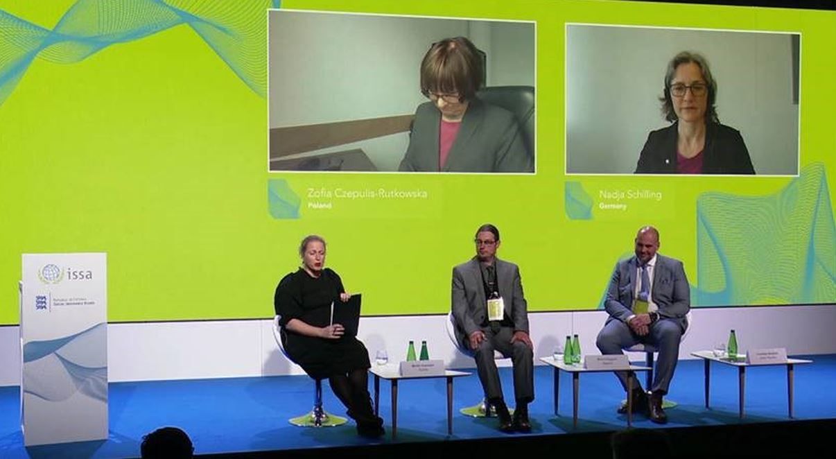 Auf dem Podium des IVSS-Forums sitzen drei Personen. Auf der Leinwand dahinter sind zwei Screens mit zugeschalteten Personen angebracht. Eine Person ist Dr. Nadja Schilling.