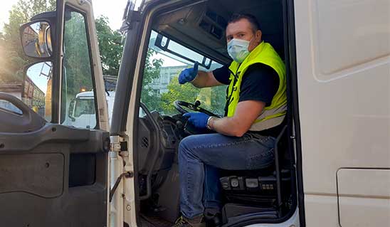 Lkw-Fahrer mit Mund-Nasen-Schutz im offenen Fahrerhaus streckt den Daumen nach oben